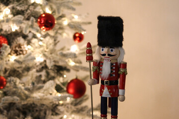Wooden nutcracker ornament beside a Christmas tree decorated with red baubles and soft glowing lights.