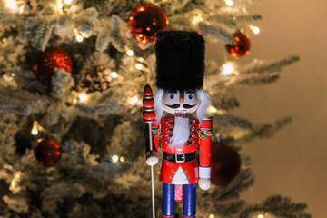 Festive wooden nutcracker figure standing before a glowing Christmas tree decorated with ornaments and lights.