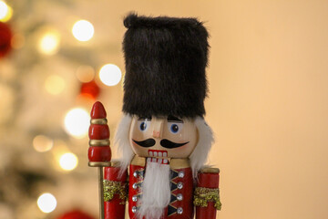 A wooden nutcracker stands beside a glowing Christmas tree decorated with classic red baubles.