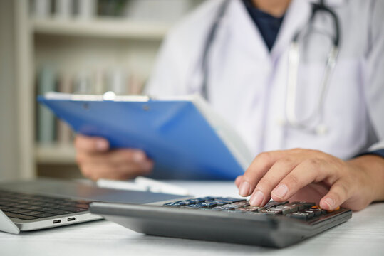Close up of doctor hand using a calculator and holding a clipboard with medical paperwork. Concept of healthcare costs, medical insurance premiums, hospital fees, and financial administration. - Powered by Adobe