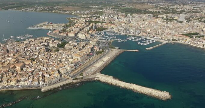 Aerial view of the island of Ortigia, in the historic centre of Syracuse, Sicily, Italy. It overlooks the sea. In the background is the city's marina and the new town. It is a sunny summer morning.