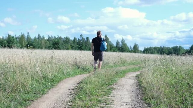 Exploring Nature a Hiker with backpack Strolling Through a Beautiful Field Beneath Vast Blue Sky. Tourist man traverses a scenic field, clear blue sky. Adventure and exploration concept. One person