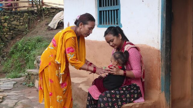 Volunteers conducting a nutritional assessment on a baby using MUAC measurement tools in a remote, traditional village setting