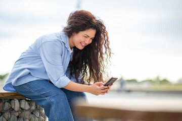 Young Asian woman smiling while texting on smartphone in relaxed outdoor setting