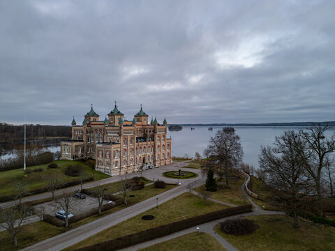 Aerial view of Stora Sundby mansion's ornate facade and lush grounds meet the serene waters under a muted sky, Stockholm, Stockholm County, Sweden.
