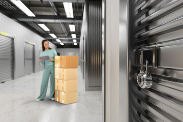Self-storage facility worker organizes delivered boxes while checking inventory on a tablet,...
