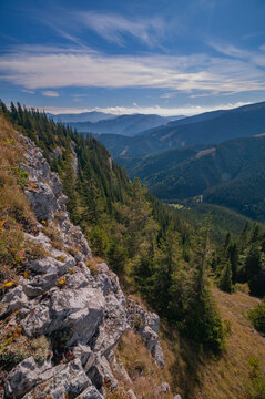 Aerial view of textured cliffs and emerald forests cascade into shadowed valleys under a bright sky, Ohniste, Zilina Region, Slovakia.