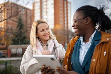 Diverse women friends talking laughing using tablet outdoors
