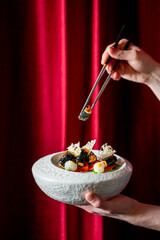 A close-up shot of hands using chopsticks to pick up a piece of gourmet, fine-dining food presented...