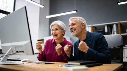 Happy senior woman and man looking at computer with credit card, celebrating online purchase success. Pension couple enjoying internet shopping.