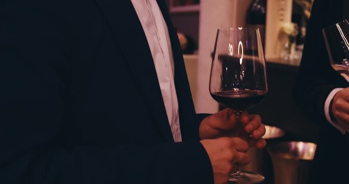 close-up view of men in formal suits and tailcoats talking while holding glasses of alcoholic beverages wine and champagne. business meeting event businessmen entrepreneurs. successful man's leisure
