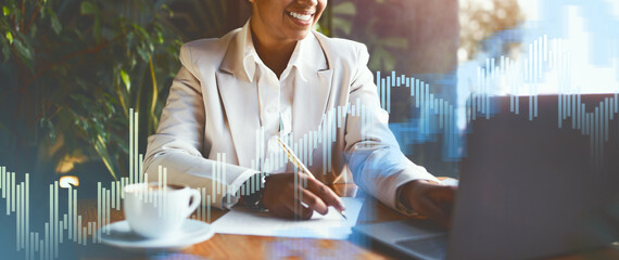 A business professional smiles as they work on a laptop, surrounded by colorful financial graphics. A warm cup of coffee sits on the table, enhancing the productive atmosphere.