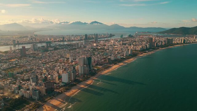 sunny sunset in Vietnamese coastal Da Nang city, My Khe sand beach and touristic My An and Son Tra district with modern skyscraper hotels and resorts, blue sea of Danang, Vietnam, aerial drone view 4k