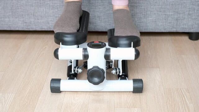 A woman in pink leggings and brown socks walks on stepper at home, front view.