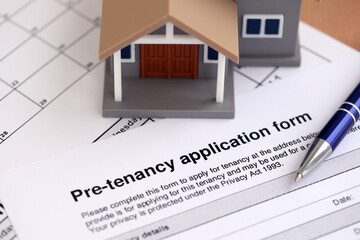 Generic toy house and Pre tenancy application form with pen on table close up