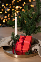 Red gift box, candle burning, fir tree composition on table with blurred golden lights on background. Still life with Christmas holiday presents