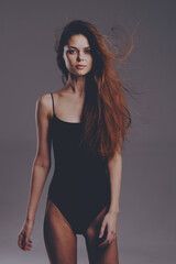 Fototapeta premium Slim woman with long hair posing in black bodysuit against gray background, showcasing elegance and natural beauty.