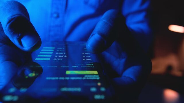 Close-up of a trader's hands buying and selling stocks on a mobile phone in a dark room