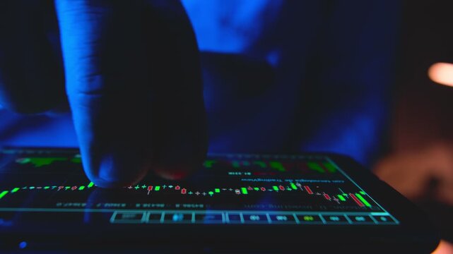 Trader's finger scrolling through a stock market financial graph on a smartphone at night