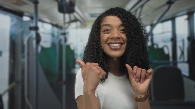 African american woman with curly hair smiles and gives thumbs up inside a city bus cabin; approval optimism.