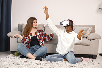 Two young teenage girls sitting on a floor near bed wearing a virtual reality glasses
