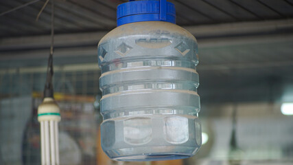 Plastic water bottle hanging on the ceiling, suspended upside down in an indoor setting with visible support.
