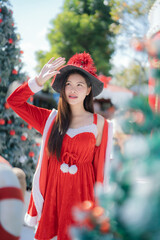 young woman dressed in a festive red Christmas outfit smiles softly. standing among beautifully decorated holiday trees.