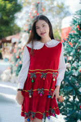 young woman dressed in a festive red Christmas outfit smiles softly. standing among beautifully decorated holiday trees.