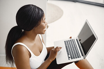 Black girl sitting on orange yoga mat in studio with big window and using a laptop