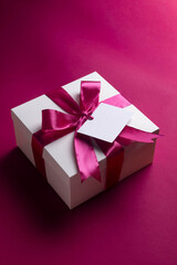 Caja de regalo blanca con lazo rosa sobre fondo rosa