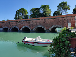 Ponte dei Voltoni bridge with boats moored along the canal in Peschiera del Garda, Italy, featuring stone arches, historic fortress town scenery, and scenic lakeside atmosphere