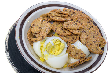 Bowl with sliced hard boiled eggs and multigrain crackers on a white background.