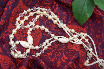 Pearl and crystal beaded necklace arranged on red patterned fabric with a green leaf.