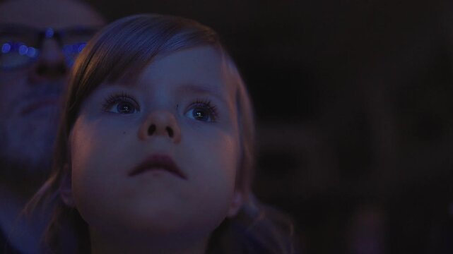 A little girl child watches a performance in the theater, a concert or a movie in the cinema very attentively. Child watching, close up face of little girl, kid eyes.