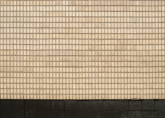 Beige ceramic mosaic wall with small square tiles and dark skirting.