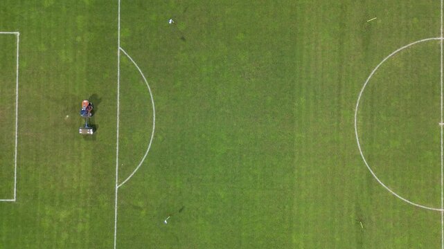 Aerial view of a football field as a groundskeeper rides a mower across the grass, maintaining the pitch with clear field markings visible