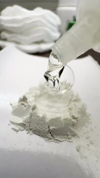 Vertical video social media - Macro closeup in a dental lab of thick specialist liquid drops from a bottle being squeezed onto a raised wall of powder, to be mixed as cement for a dental procedure.