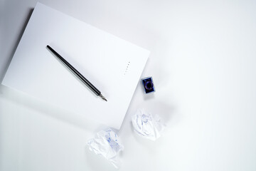 A top-down view of a blank sheet of paper, a black nib pen, an inkwell with blue ink