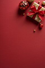 A vertical festive red background with a wrapped gift, red bow, and decorative ornaments evokes...