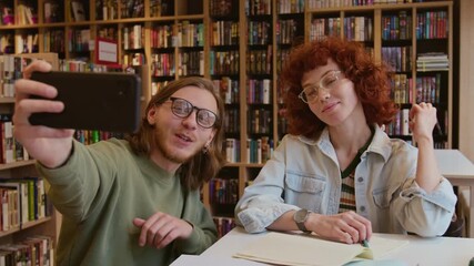Two cheerful young college students taking selfie photo on smartphone, making peace sign and smiling while meeting in library for study session - Powered by Adobe