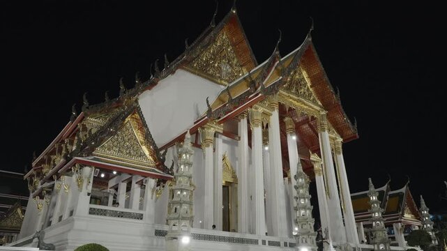 Beautiful traditional Thai temple architecture with pointed roofs glowing against the dark night sky.