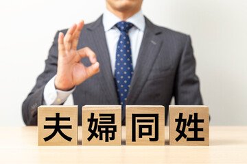 Obraz premium 「夫婦同姓」と書かれたブロックとOKポーズをするビジネスマン