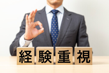 「経験重視」と書かれたブロックとOKポーズをするビジネスマン