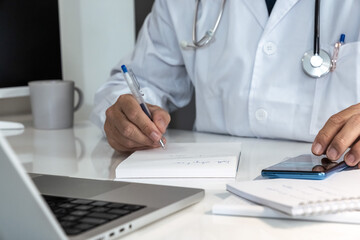 Healthcare professional in lab coat diligently working on a laptop, with stethoscope nearby,...