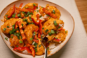Close up view of spicy chicken with rice, red pepper slices, and green onions served in a bowl