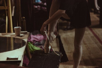 Ballet dancer adjusting pointe shoes backstage during final theater rehearsal. Concept of technical readiness, careful gear preparation and structured routine before performance.