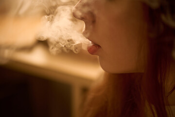 Caucasian young adult woman exhaling vapor from mouth, closeup showing side of face and lips with...