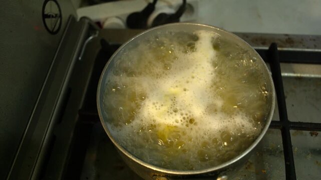 Close-up isolated gritty every day style grunge dark documentary shot of penne pasta boiling in a saucepan with water bubbling on the surface