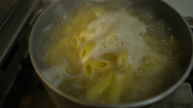 Close-up isolated gritty every day style grunge dark documentary shot of penne pasta boiling in a saucepan with water bubbling on the surface