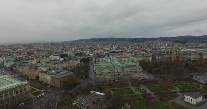 Wide aerial panorama of the historic center of Vienna, Austria, showing a large urban park Volksgarten and massive, neoclassical government buildings Parliament under an overcast, winter sky.